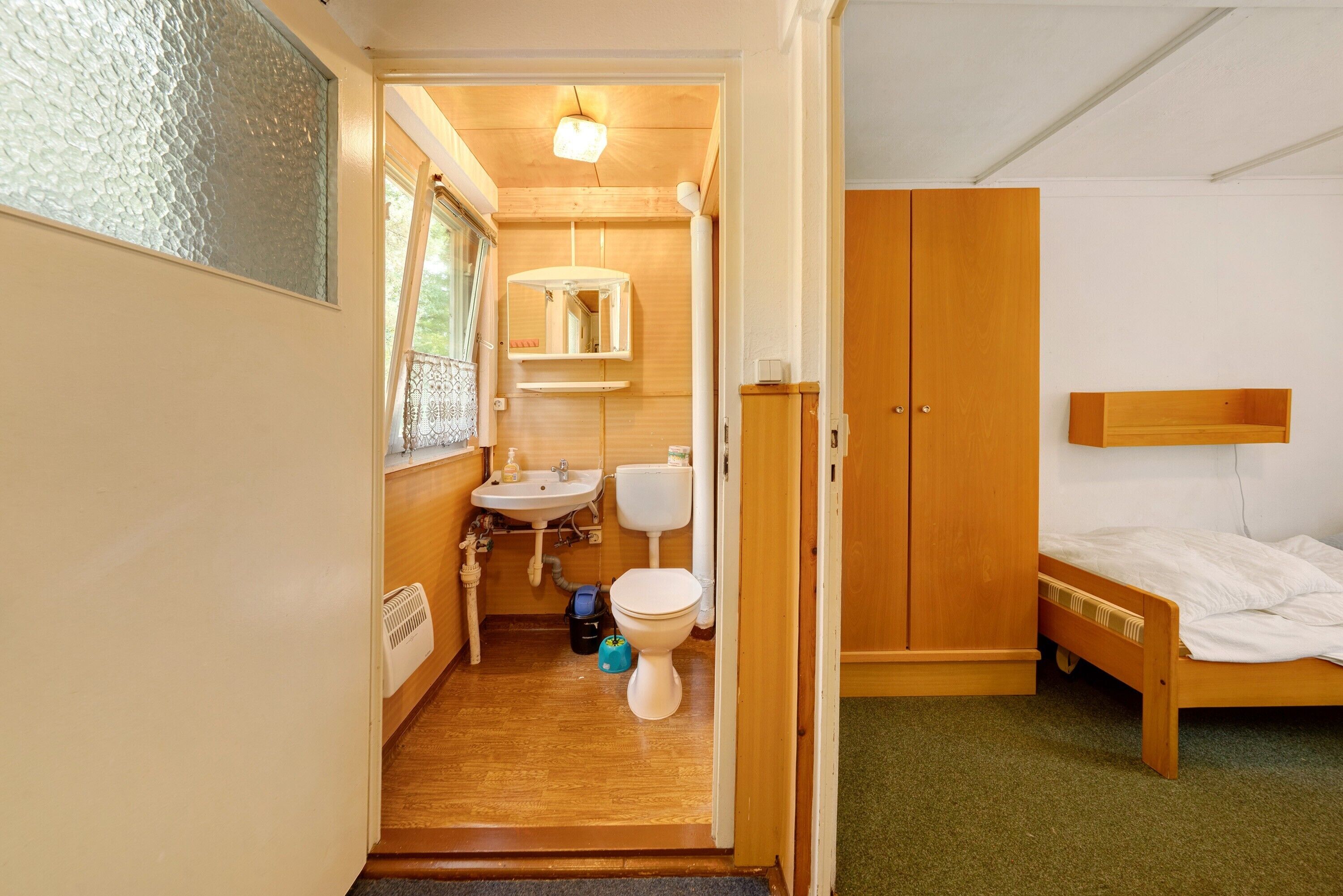 Une petite pièce comprenant un lit en bois, un petit lavabo et des toilettes.