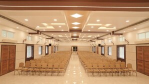 Une grande salle de conférence avec des rangées de chaises, un plancher ciré et un design de plafond moderne.