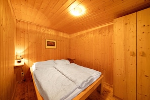 Une pièce aux murs lambrés, comprenant un lit, une table de chevet et une lampe fixée au mur.