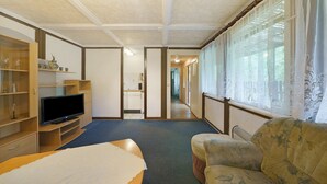 Una habitación con cama, televisor, sofá y ventana con cortinas translúcidas.
