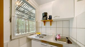 A kitchen with a window, a stove, a sink, and a shelf with a coffee maker.