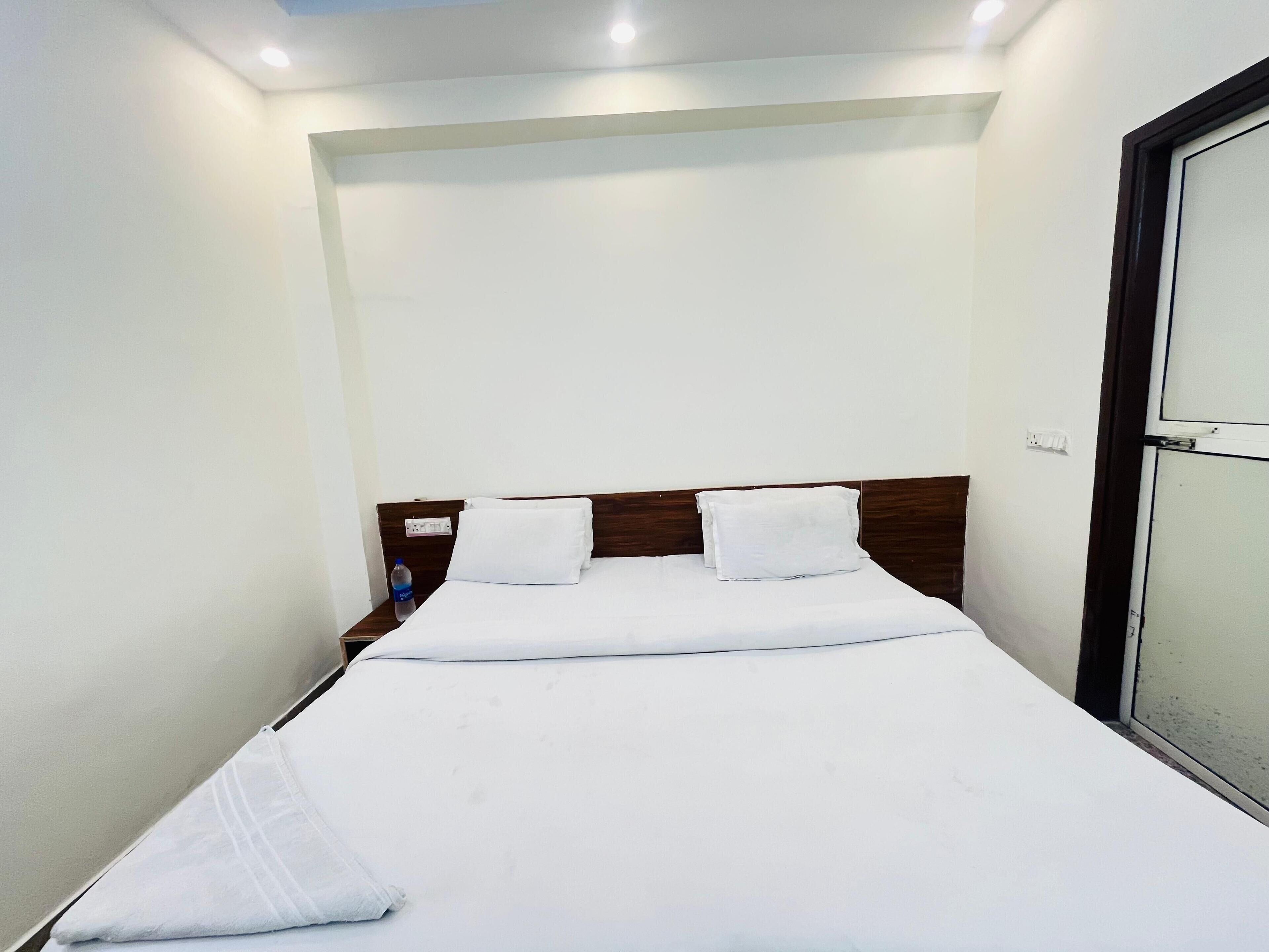A neatly made bed with white linens and pillows, a wooden headboard, and a water bottle on the nightstand.