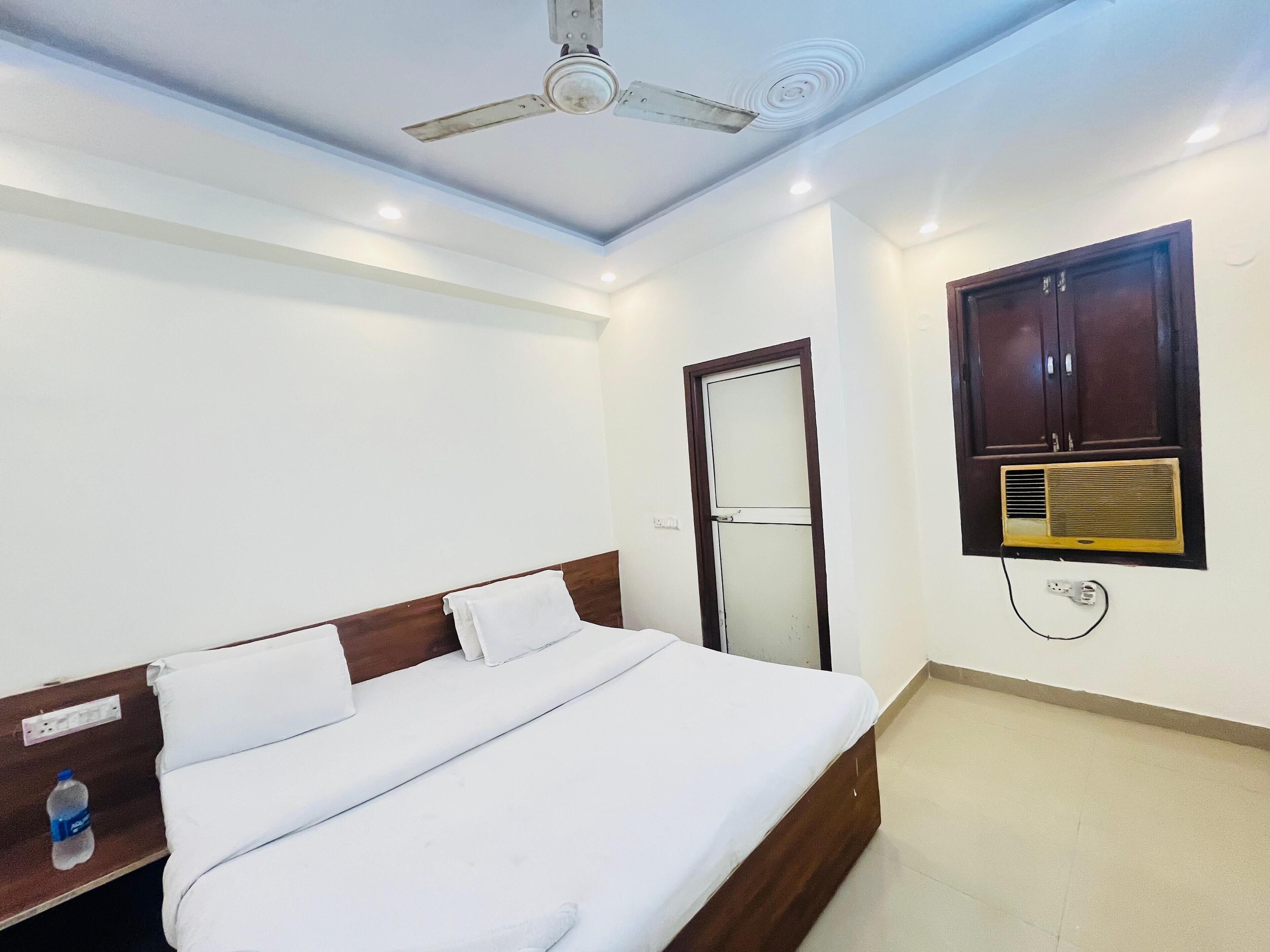 A hotel room with a bed, a ceiling fan, a wall-mounted air conditioner, and a door.