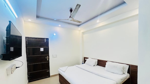 A modern hotel room with a bed, a ceiling fan, a TV mounted on the wall, and a door with a shelf. - Roomshala Hotel Pub G (New Delhi)