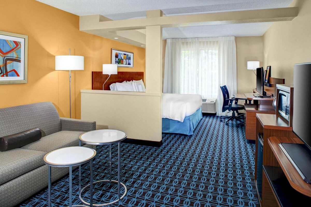 A hotel room with a sofa, two small tables, a bed with a white comforter, a desk with a computer, and a TV.