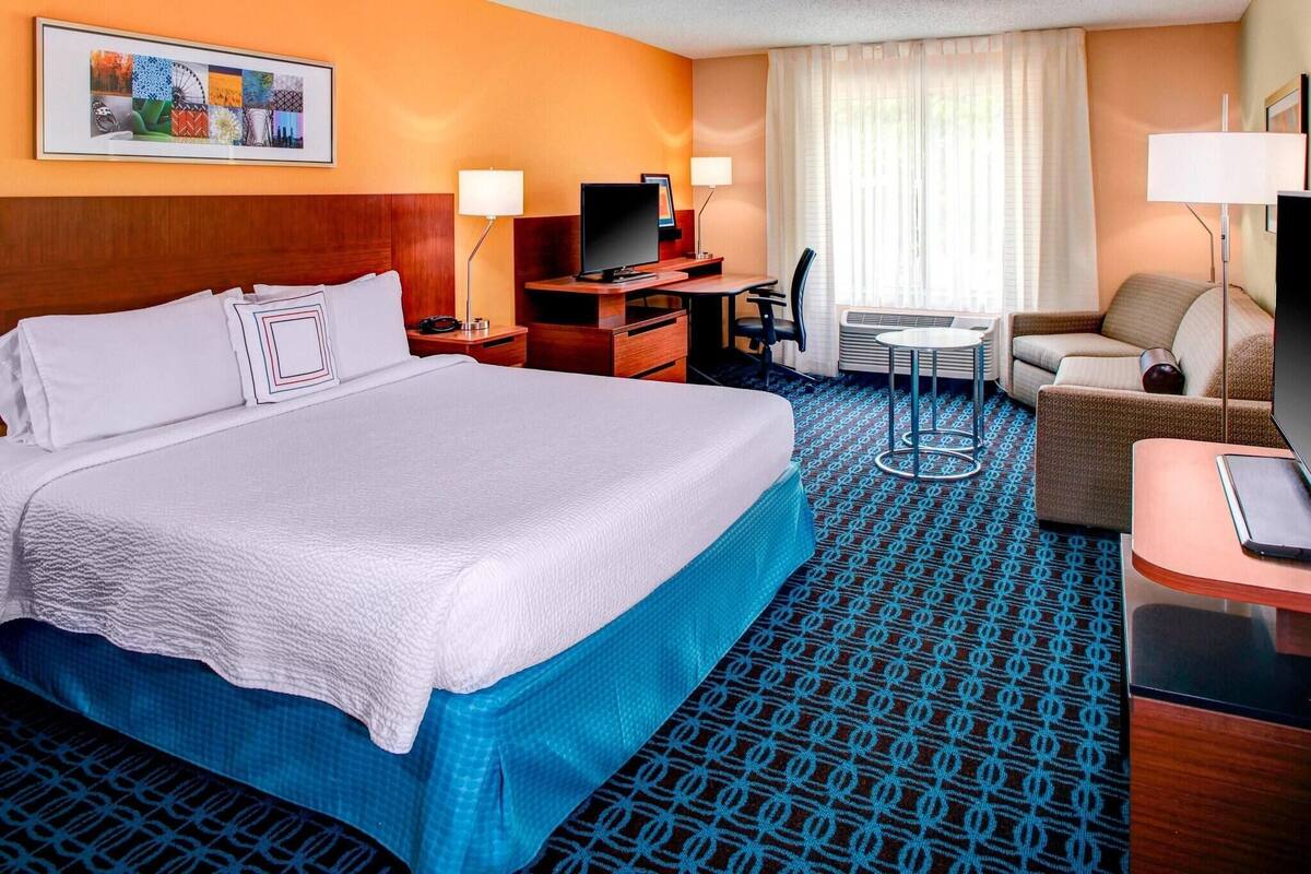 Une chambre d’hôtel avec un grand lit, un bureau avec un ordinateur, une télévision, une chaise et un canapé.
