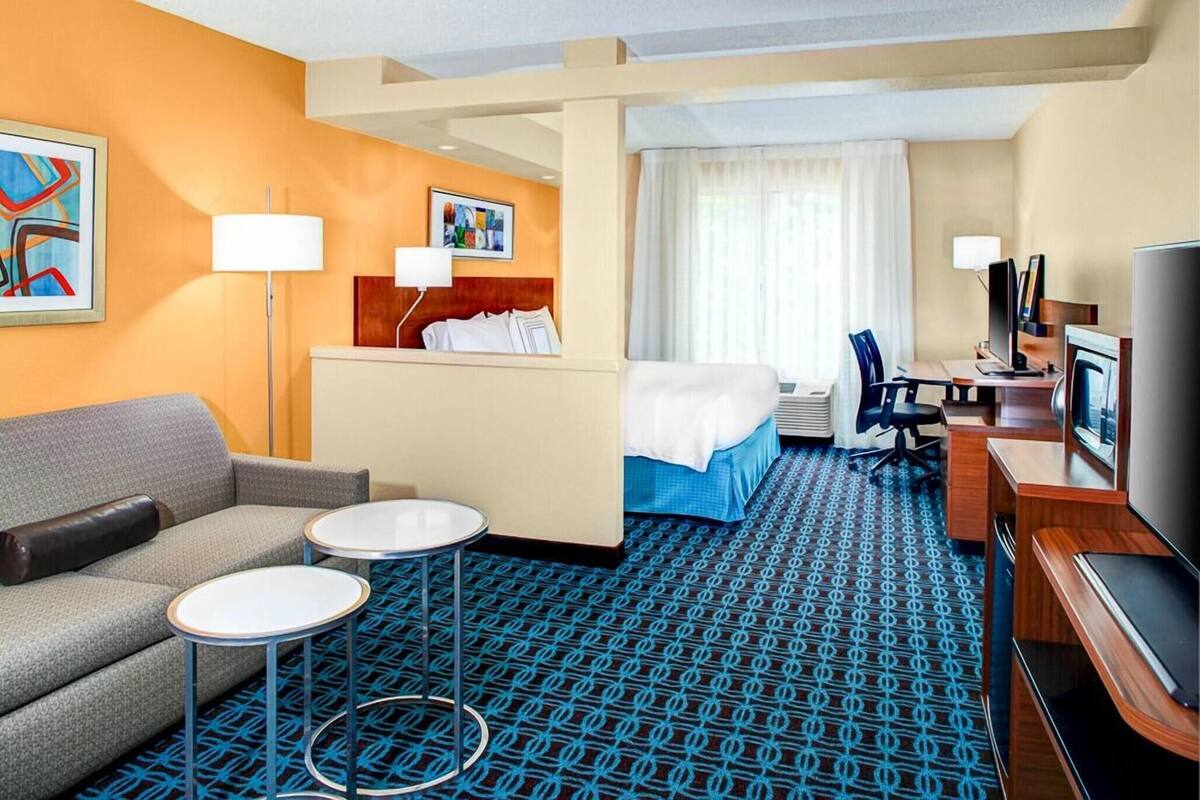 Une chambre d’hôtel avec un lit, un canapé, un bureau avec un ordinateur, une télévision et une moquette à motifs.