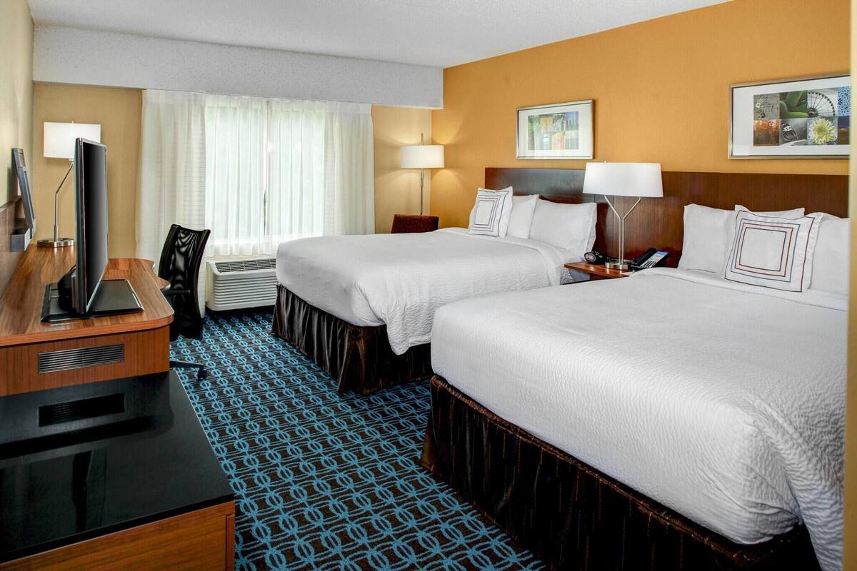 Une chambre d ’hôtel avec deux lits, un bureau avec un ordinateur, une télévision et une fenêtre avec des rideaux.
