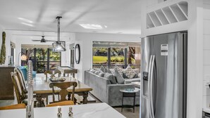 Una cocina moderna con comedor, un amplio ventanal con vistas a la vegetación y un refrigerador de acero inoxidable.