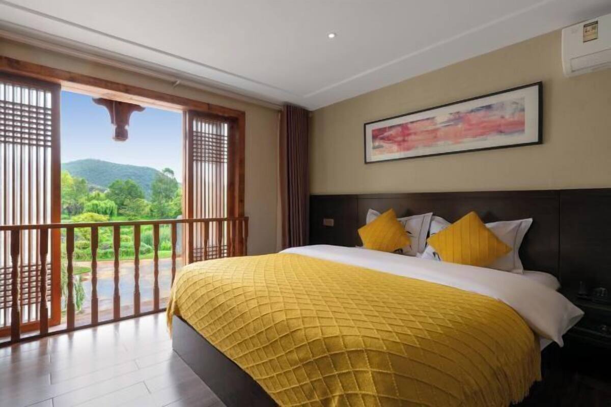 Een hotelkamer met een bed, een schilderij aan de muur en uitzicht op groen door het raam.
