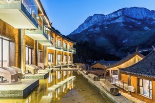 Un edificio tradicional con un estanque reflectante, un paisaje montañoso al fondo y cielo despejado.
