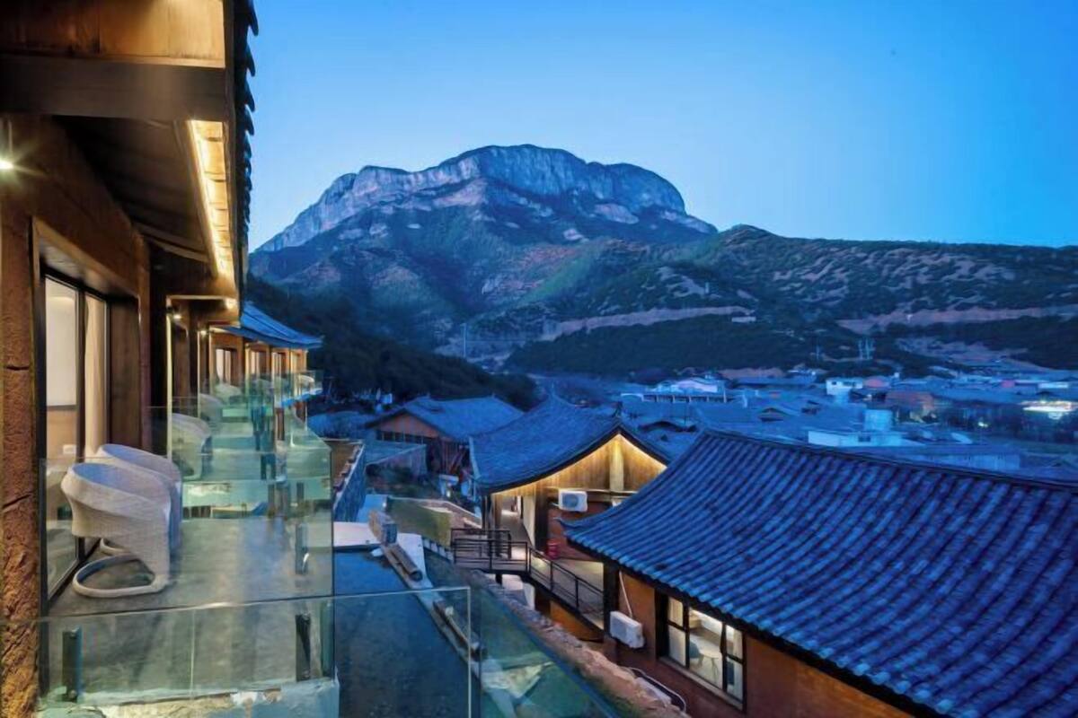 Een hotel met een glazen balkon met uitzicht op een berg, traditionele architectuur en een panorama van het omliggende dorp.