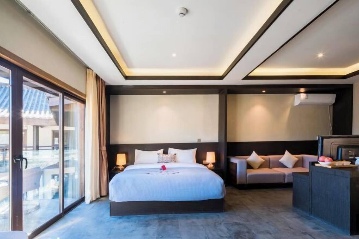 Een moderne hotelkamer met een groot bed, een bank, een bureau en een schuifdeur naar buiten.
