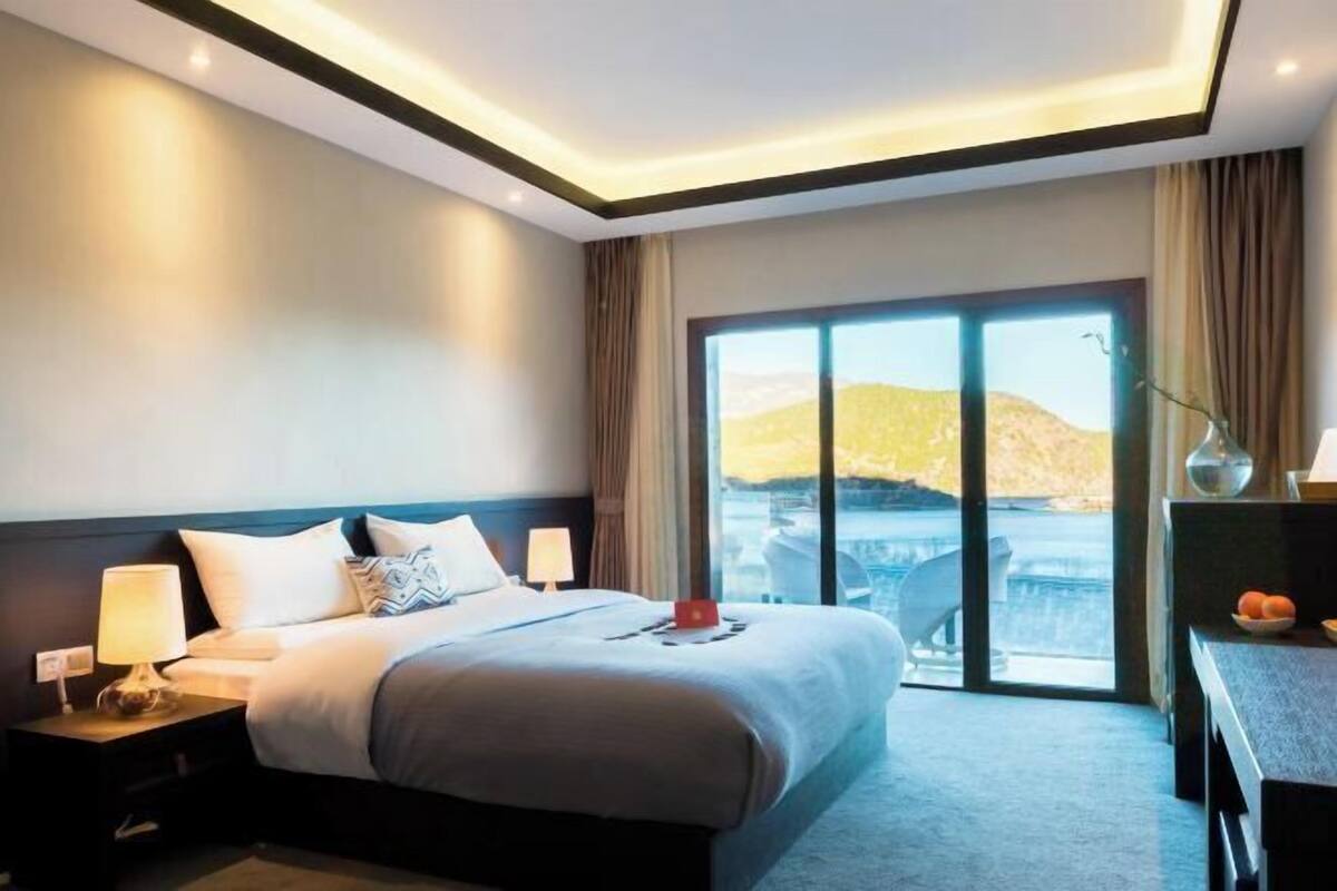 Hotelkamer met een groot bed, een bureau, een stoel en uitzicht op een landschap door een groot raam.