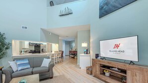 Una sala de estar moderna con sofá, mesa de centro, televisor y área de cocina.