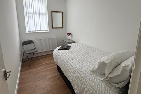 A bedroom with a bed, a chair, a radiator, a small table with a vase of flowers, and a mirror on the wall. - 2 Bed Flat - Sleeps 3 - Parking - Wifi (South Shields)