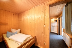 A wooden room with a bed, a small kitchenette, and a door leading to another room.