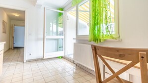 Ein Zimmer mit Fliesenboden, einem Holzstuhl, einem Heizkörper und einem Fenster mit grünen Vorhängen.