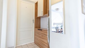 Ein schmaler Gang mit einer weißen Tür, Holzschränken und einem Kühlschrank.