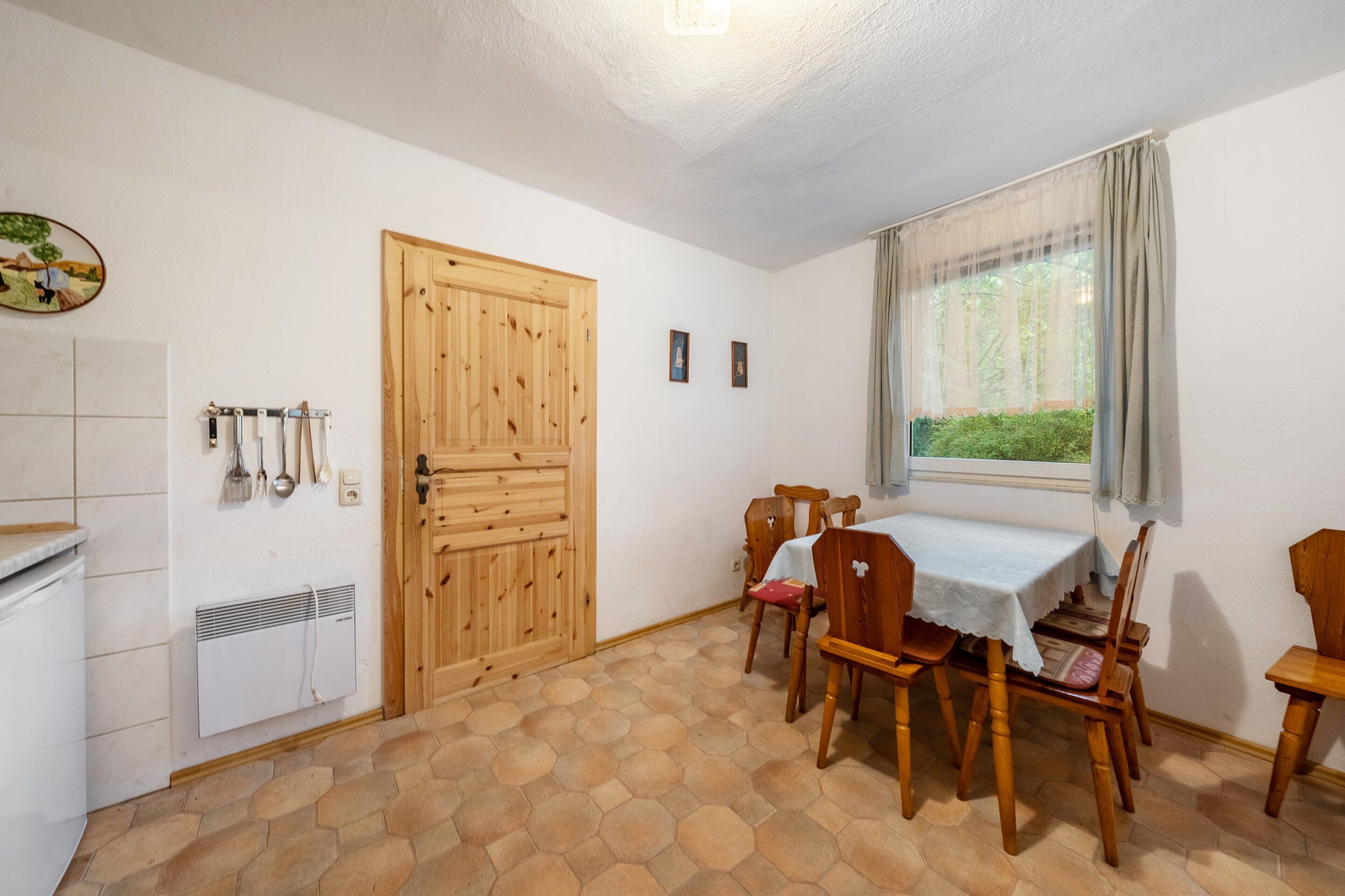 Un comedor con una mesa y sillas, una puerta de madera, una ventana con cortinas y un radiador en la pared.
