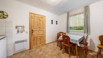 Un comedor con una mesa y sillas, una puerta de madera, una ventana con cortinas y un radiador en la pared.