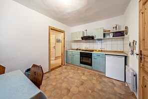 Cozinha compacta com piso em azulejo, armários de madeira, forno embutido e uma geladeira pequena.