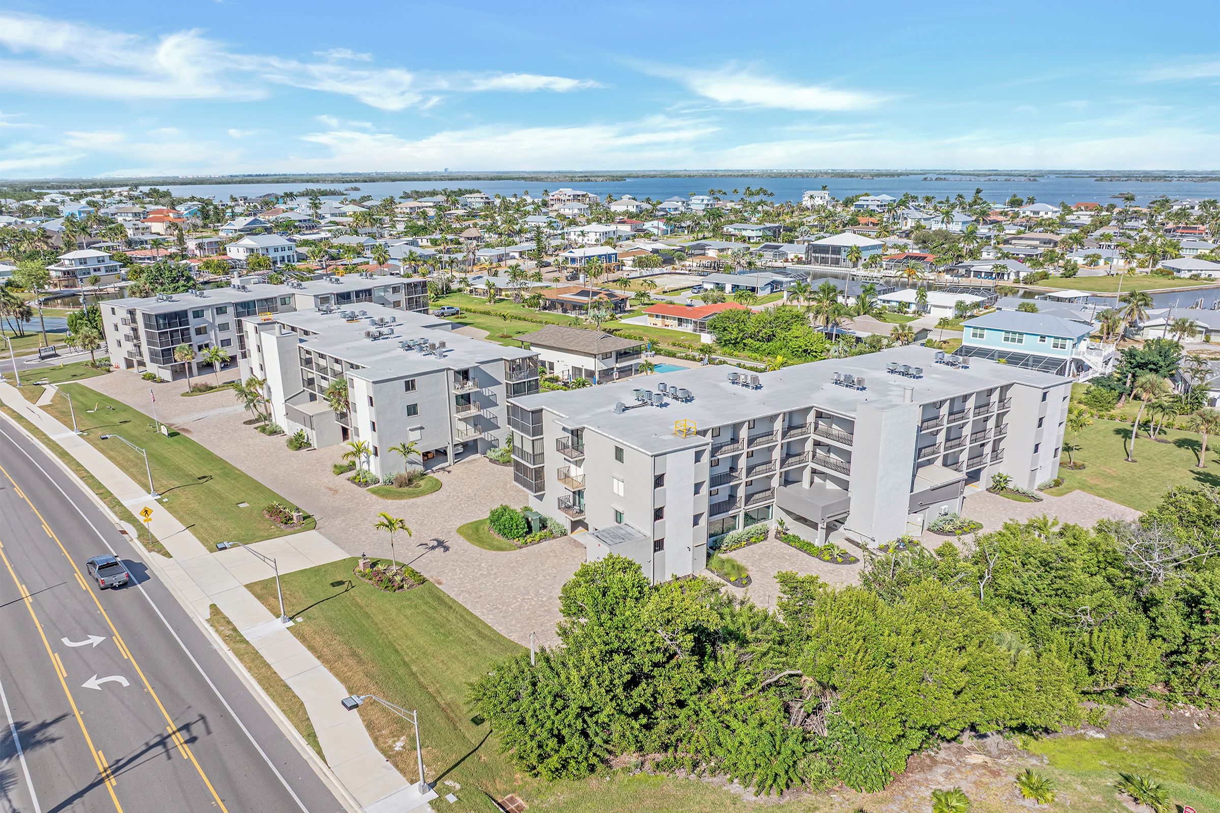 Un quartier résidentiel avec des immeubles d’appartements modernes, une route dotée d’un passage piéton et une étendue d’eau en arrière-plan.