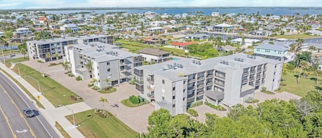 A residential area with modern apartment buildings, a road with a pedestrian crossing, and a body of water in the background.