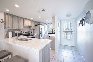 A modern kitchen with a central island, stainless steel appliances, and a view to the outside. - SUMMER SPECIAL DISCOUNT!!!  2B/2B Fairview Isles 214 Condo, Walk to Beach, Heated Pool! (Fort Myers Beach)