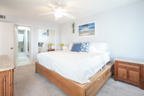 A bedroom with a bed, a nightstand, a wooden cabinet, a ceiling fan, and a beach-themed wall art. - 2B/2B Fairview Isles 214 Condo, Walk to Beach, Heated Pool! (Fort Myers Beach)