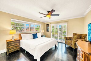 A bedroom with a bed, a nightstand, a lamp, a ceiling fan, a leopard print chair, and a sliding glass door leading to a balcony.