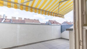 A balcony with a striped awning, tiled floor, and a view of neighboring buildings.
