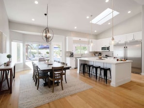 Una cocina moderna con una isla central, muebles blancos y electrodomésticos de acero inoxidable.