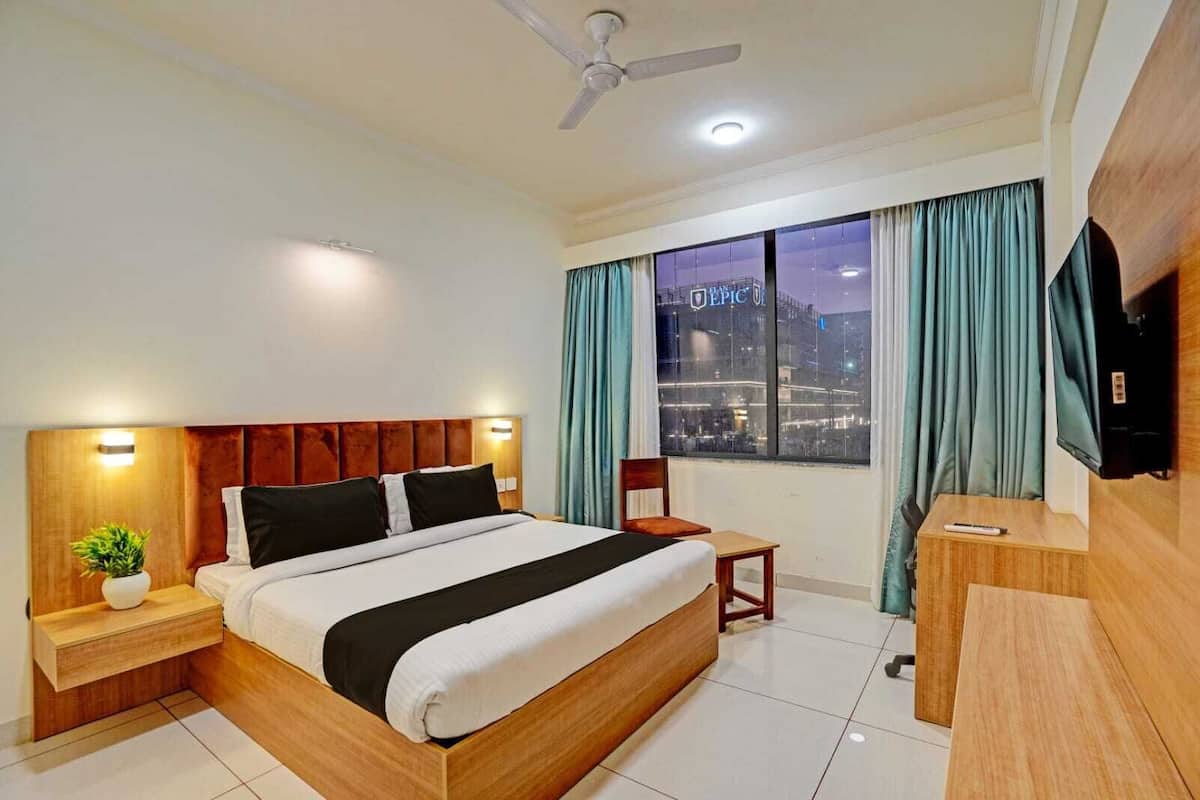 A hotel room with a bed, a desk, a chair, a TV, a ceiling fan, and a window with curtains.