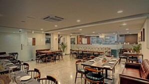 A spacious restaurant with multiple dining areas, including booths and tables, and a view of the city through large windows. - Hotel RR Galaxy (Gurugram)