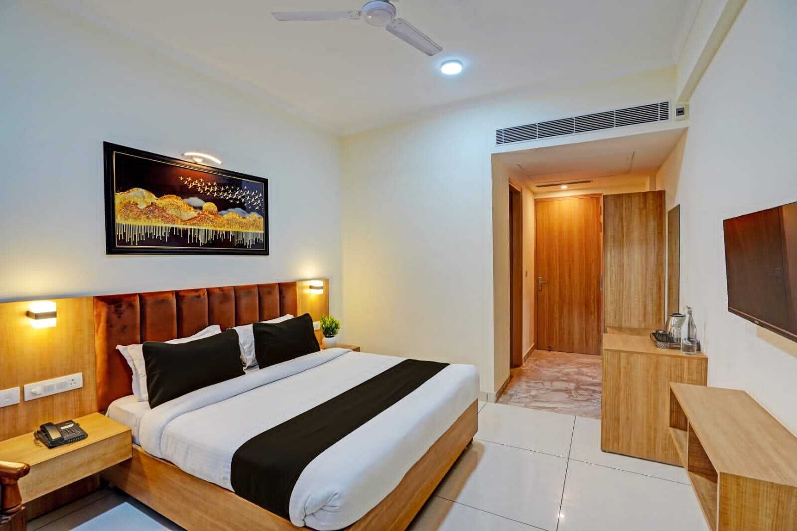 Een hotelkamer met een bed, nachtkastjes, een televisie, een schilderij en een houten deur.