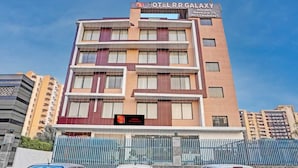 A multi-story hotel building with a sign indicating it has rooms, banquets, and a restaurant. There are three cars parked in front. - Hotel RR Galaxy (Gurugram)