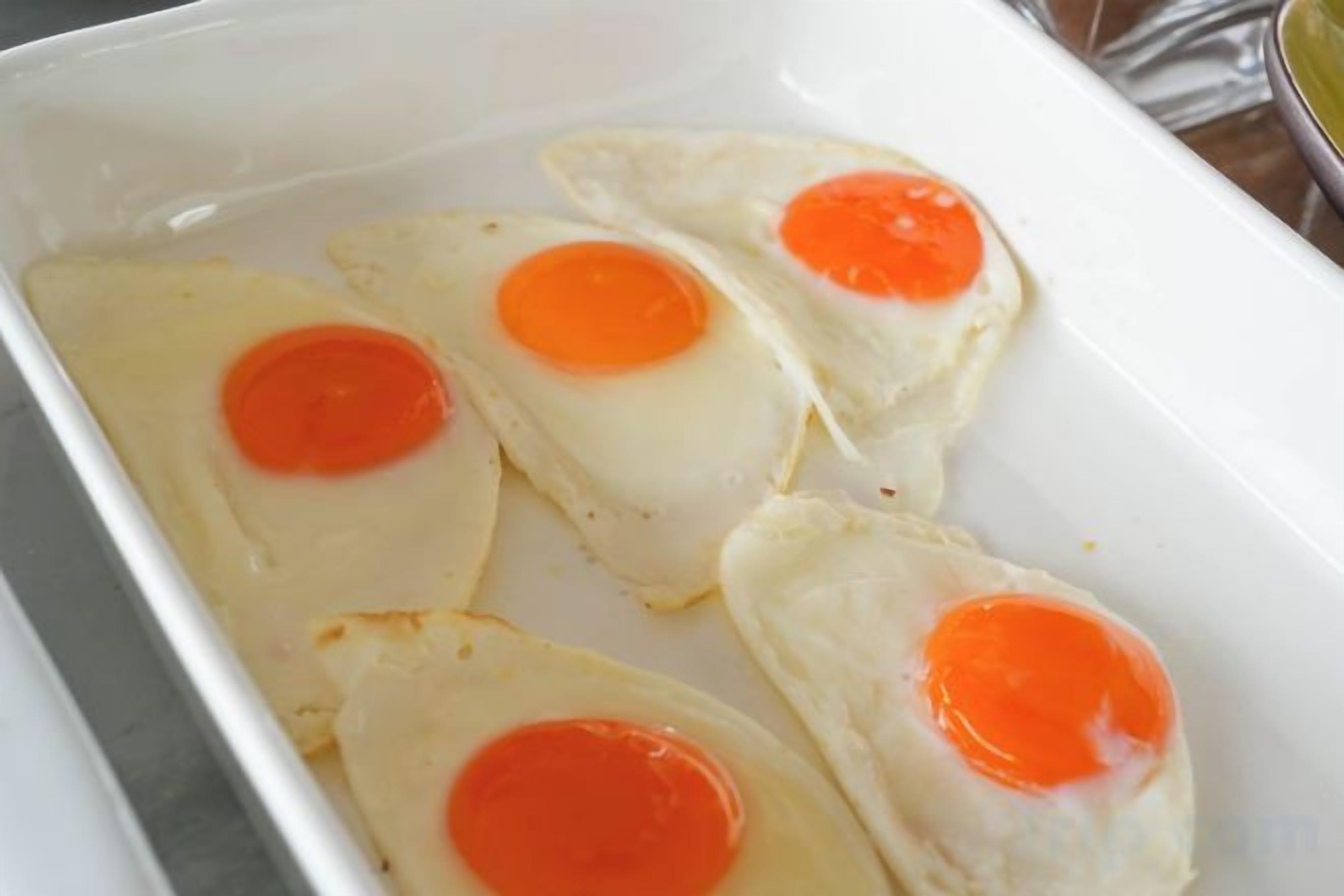 A white rectangular dish containing four fried eggs with runny yolks.