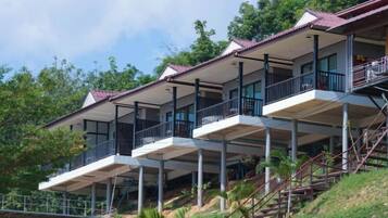 A multi-story building with balconies, a staircase, and a view of the surrounding greenery.
