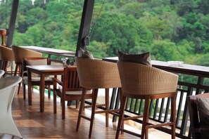 A terrace with wicker chairs and a table, overlooking a forested area. - So View Phuket Resort (Phuket)