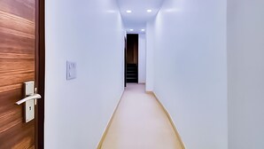 Un couloir étroit aux murs blancs, avec une porte en bois sur le côté gauche.