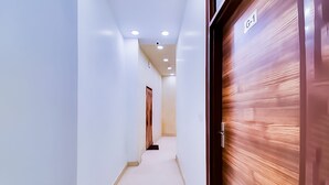 Un couloir aux murs blancs, une porte en bois portant l’inscription « G-1 », et des spots encastrés au plafond.