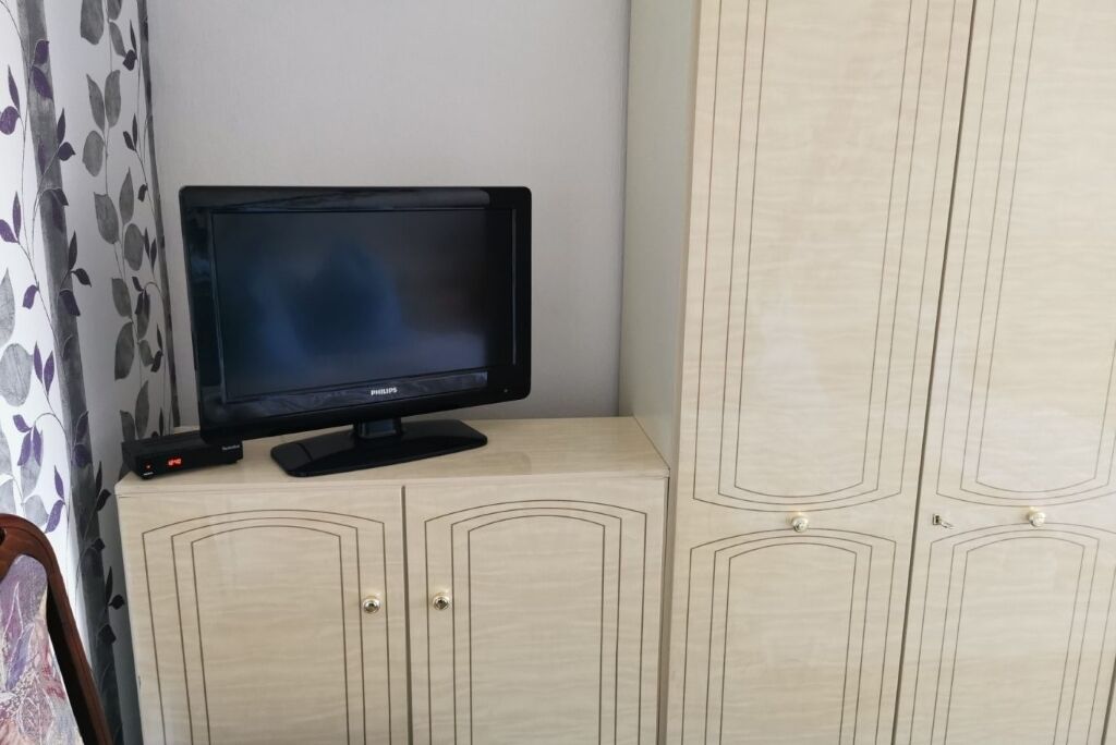 A television on a cabinet with a floral curtain in the background.