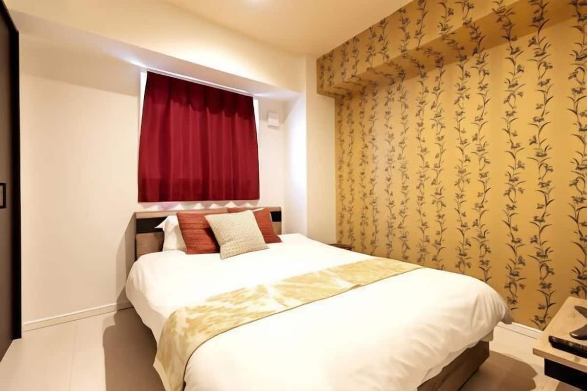 Una habitación de hotel con una cama grande, cortinas rojas, papel tapiz floral y una mesita de noche pequeña.