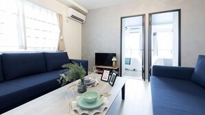 A modern living room with a sofa, a dining table set with plates and glasses, a television, and a sliding door leading to another room. - Ra Premier K (Osaka)