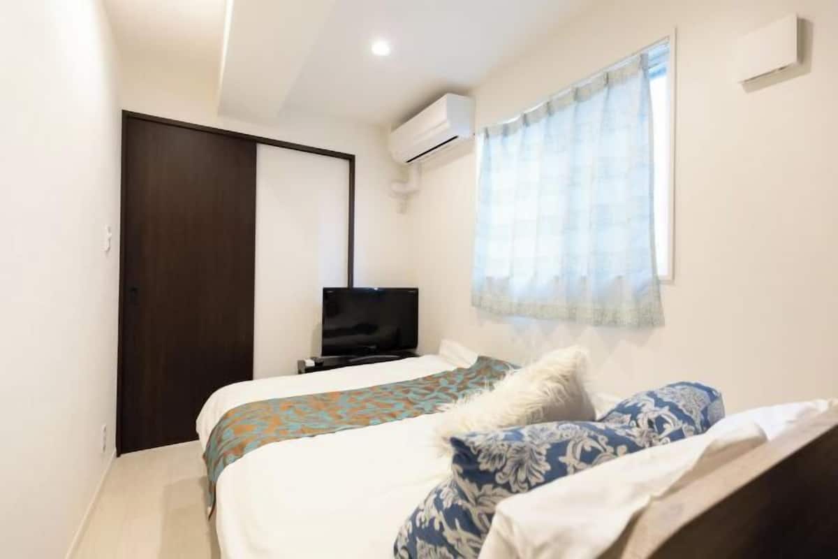 Una habitación de hotel con cama, televisor, aire acondicionado y ventana con cortinas.