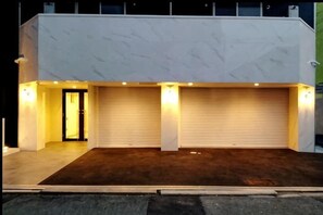 En moderne bygning med garageport, indkørsel og oplyst indgang.