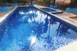 A rectangular swimming pool with blue mosaic tiles and a clear water surface reflecting trees. - Little Yellow House • Insta: @little.yellow.house1943 (Cansaulim)