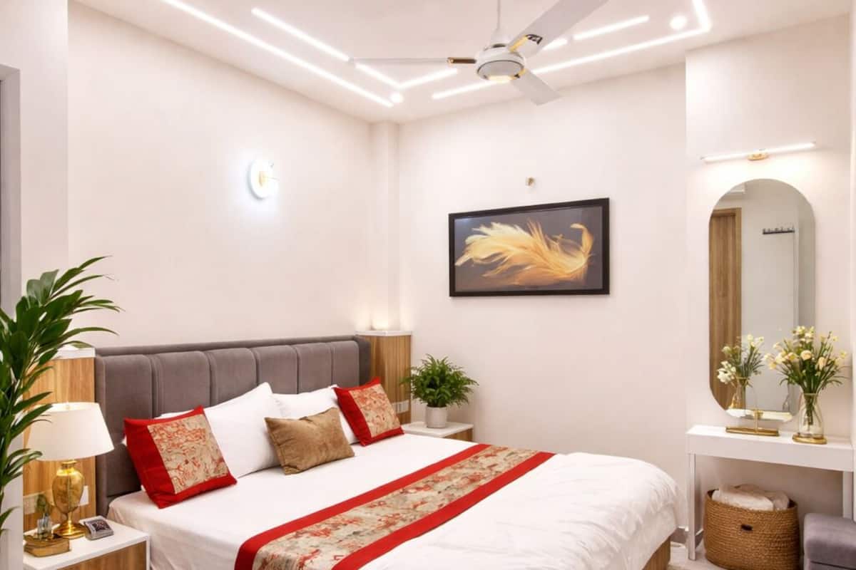A modern bedroom with a bed, bedside tables, a nightstand, a ceiling fan, a wall-mounted TV, and a mirror.