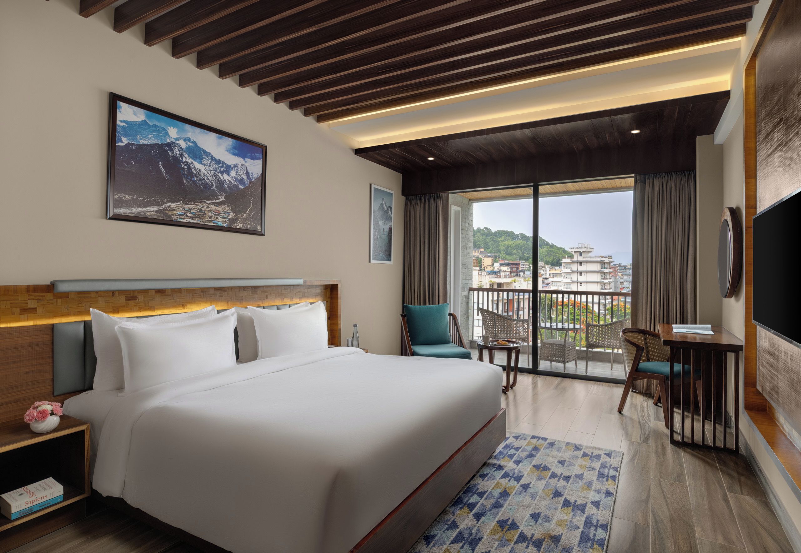 A hotel room with a large bed, a view of the city through a balcony, and a mounted television.
